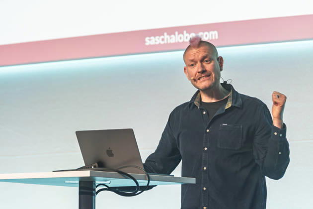Berlin, 16.10.2026: Auf der NeulandPro Connect 2026 ballt der Publizist und Digital-Vordenker Sascha Lobo während seines Vortrags am Rednerpult die Faust. Die zweitägige KI-Konferenz NeulandPro Connect 2026 findet am 16. und 17. Oktober im Westhafen Event & Convention Center (WECC) in Moabit statt, einem historischen Speichergebäude am Berliner Westhafen. Veranstalter ist NeulandPro, eine Bildungs- und Medienmarke rund um Künstliche Intelligenz. Mit Vorträgen, Workshops und Hackathons richtet sich die Konferenz vor allem an kleine und mittelständische Unternehmen, Gründer und Führungskräfte, die KI praktisch einsetzen wollen; erwartet werden bis zu 1.000 Gäste. NeulandPro Connect 2026 - KI-Konferenz in Berlin