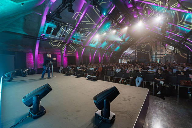 Berlin, 16.10.2026: Blick von der Bühne in die violett und türkis beleuchtete Halle des WECC: Der Publizist und Digital-Vordenker Sascha Lobo spricht am Rednerpult vor dem Publikum der NeulandPro Connect 2026. Die zweitägige KI-Konferenz NeulandPro Connect 2026 findet am 16. und 17. Oktober im Westhafen Event & Convention Center (WECC) in Moabit statt, einem historischen Speichergebäude am Berliner Westhafen. Veranstalter ist NeulandPro, eine Bildungs- und Medienmarke rund um Künstliche Intelligenz. Mit Vorträgen, Workshops und Hackathons richtet sich die Konferenz vor allem an kleine und mittelständische Unternehmen, Gründer und Führungskräfte, die KI praktisch einsetzen wollen; erwartet werden bis zu 1.000 Gäste. NeulandPro Con