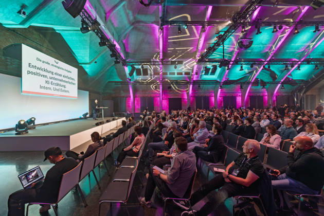 Berlin, 16.10.2026: Teilnehmerinnen und Teilnehmer der NeulandPro Connect 2026 verfolgen in der Halle des WECC den Vortrag von Sascha Lobo, Publizist und Digital-Vordenker; auf der Leinwand die Folie Entwicklung einer einfachen, positiven, unternehmerischen KI-Erzählung. Intern. Und Extern. Die zweitägige KI-Konferenz NeulandPro Connect 2026 findet am 16. und 17. Oktober im Westhafen Event & Convention Center (WECC) in Moabit statt, einem historischen Speichergebäude am Berliner Westhafen. Veranstalter ist NeulandPro, eine Bildungs- und Medienmarke rund um Künstliche Intelligenz. Mit Vorträgen, Workshops und Hackathons richtet sich die Konferenz vor allem an kleine und mittelständische Unternehmen, Gründer und Führungskräfte, die