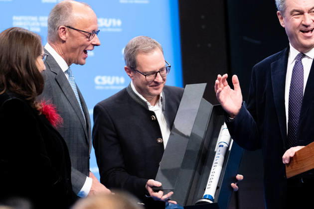 Tag 2, Parteitag 2026 der Partei CSU (Christlich-Soziale-Union) in der Messe München. Generalsekretär Martin Huber und Ministerpräsident Dr. Markus Söder überreichen Friedrich Merz (Bundeskanzler BRD Bundesrepublik Deutschland, CDU) eine Miniatur-Rakete von ISAR AEROSPACE