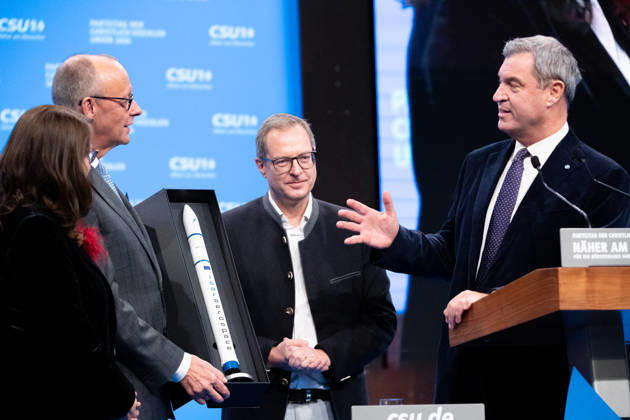 Tag 2, Parteitag 2026 der Partei CSU (Christlich-Soziale-Union) in der Messe München. Generalsekretär Martin Huber und Ministerpräsident Dr. Markus Söder überreichen Friedrich Merz (Bundeskanzler BRD Bundesrepublik Deutschland, CDU) eine Miniatur-Rakete von ISAR AEROSPACE