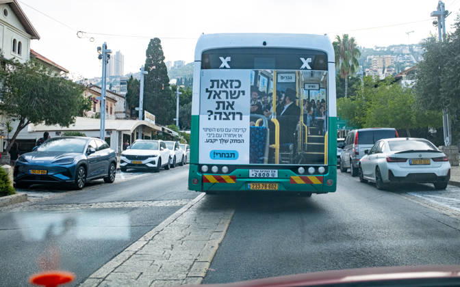 Wahlen in Israel 2026. Israel, Haifa am 24. Oktober, 2026: Ein Linienbus des öffentlichen Nahverkehrs in Haifa mit einem großflächigen Wahlkampfaufkleber auf der Rückseite. Das Motiv zeigt orthodoxe jüdische Männer im vorderen Bereich eines Busses unter einem Schild mit der Aufschrift Männer, während junge säkulare Frauen im hinteren Bereich unter einem Schild Frauen sitzen. Der Slogan lautet sinngemäß: Willst du ein Israel wie dieses? Vorwärts mit dem Block des Wandels oder rückwärts mit Bibi (Benjamin Netanjahu). Deine Stimme entscheidet. Wähle! (in der weiblichen Form.)