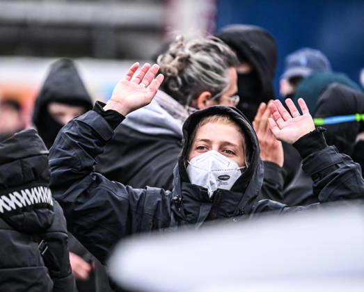 A young blonde woman wearing a black hood and a face mask raises both hands conspicuously during a student protest in central Brussels, Belgium, on 24 October 2026. The gesture takes place amid demonstrations and repeated police interventions in the city centre.