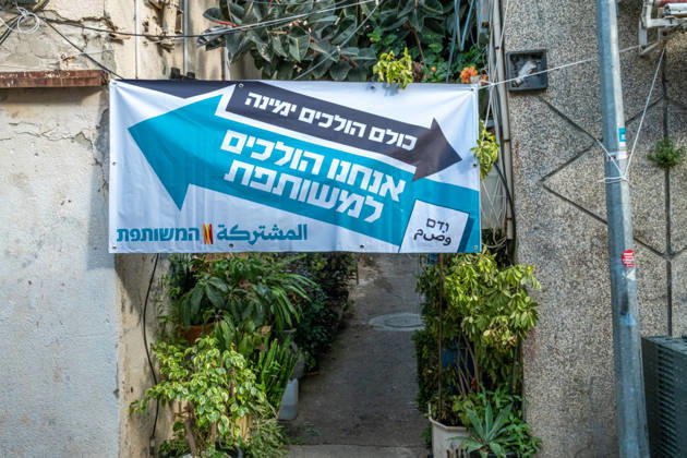 Wahlen in Israel 2026. Israel, Haifa am 24. Oktober, 2026: Wahlplakat der arabischen Parteienallianz Vereinte Liste ,gespannt zwischen zwei Mauern einer begrünten Gasse im überwiegend von arabischen Bürgern bewohnten Stadtteil Wadi Nisnas in Haifa. Der Slogan lautet auf Hebräisch: Alle gehen (Richttung) Rechts, wir gehen zu der Vereinten.